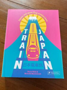Dunkelrot Rezi Train Japan. Das Cover zeigt grafische Elemente unter anderem einen Zug, der aus einem Tunnel kommt. Farbschema ist bunt.