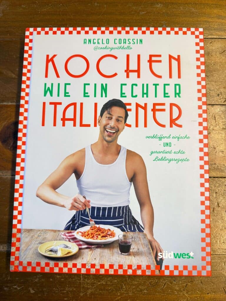 Kochen wie ein Italiener von Angelo Coassin Cover zeigt Mann mit einem ärmellosen Top und Pasta Rezi auf dunkelrot.de