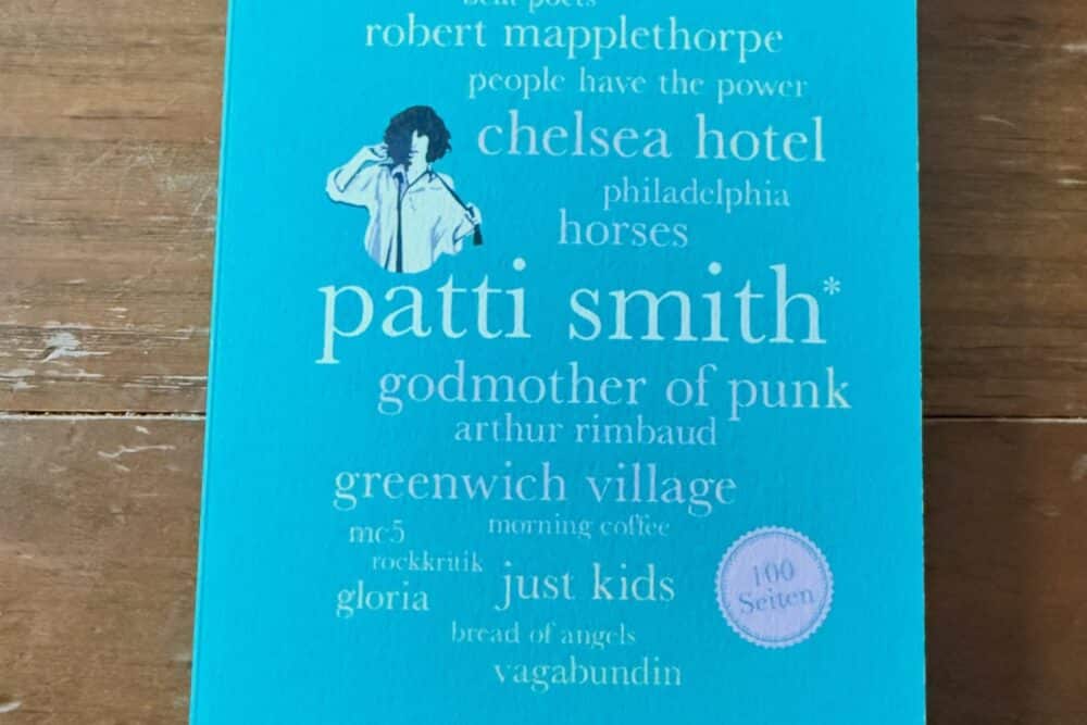 Patti Smith 100 Seiten Rezension: Cover des Buches von Kersty und Sandra Grether, erschienen bei Reclam, auf Holztisch fotografiert