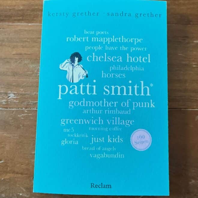 Patti Smith 100 Seiten Rezension: Cover des Buches von Kersty und Sandra Grether, erschienen bei Reclam, auf Holztisch fotografiert