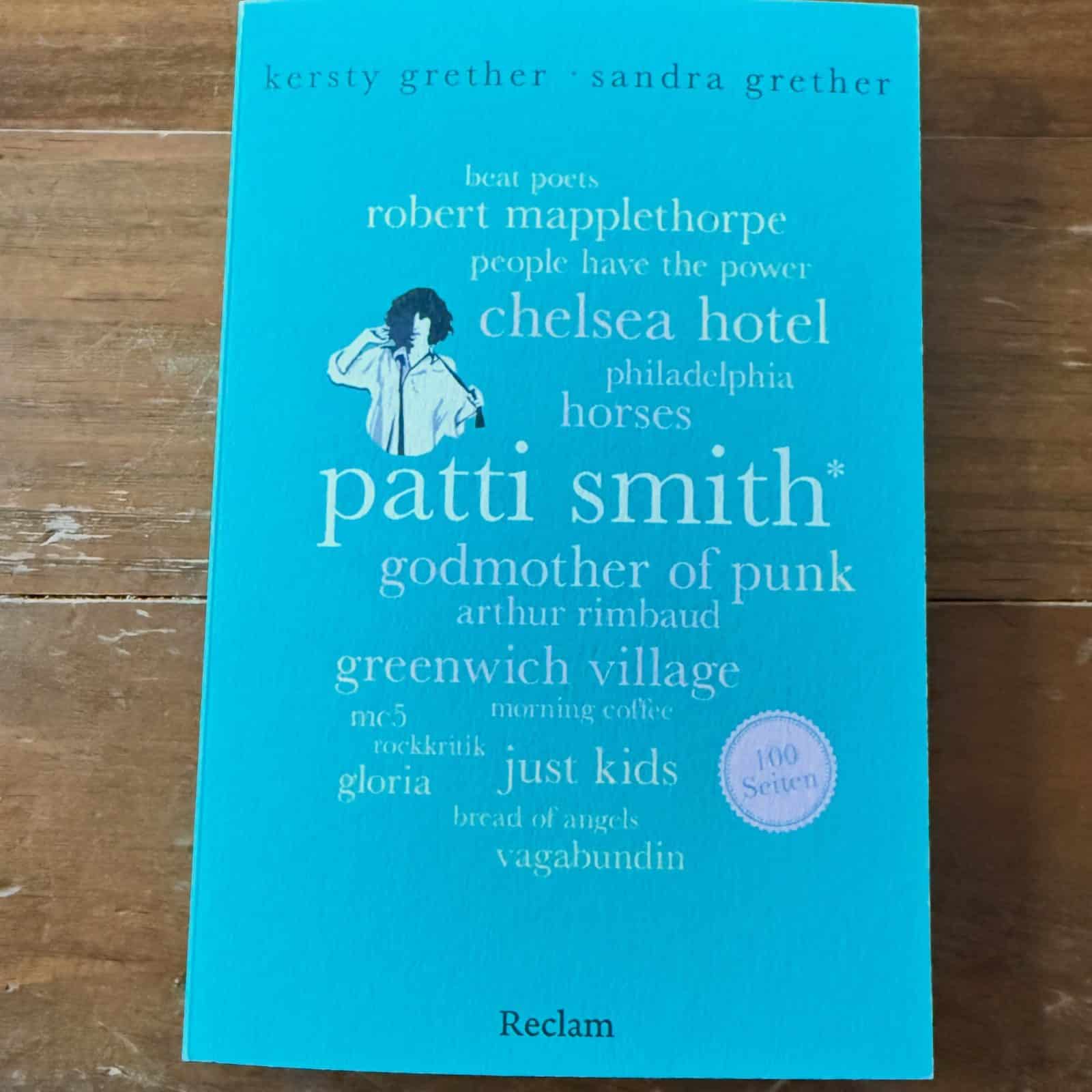 Patti Smith 100 Seiten Rezension: Cover des Buches von Kersty und Sandra Grether, erschienen bei Reclam, auf Holztisch fotografiert