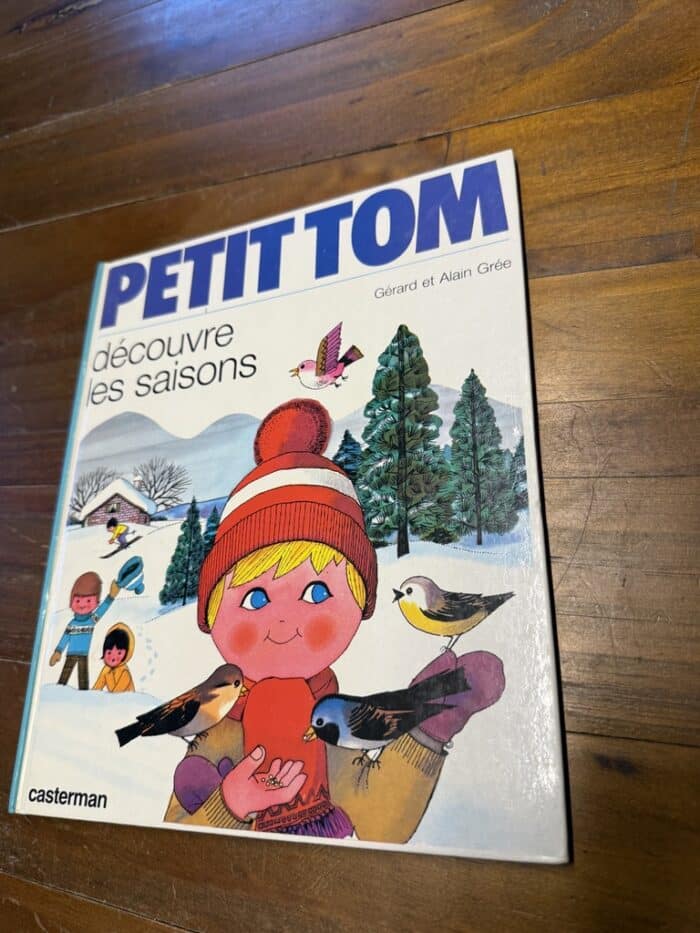 Cover von Petit Tom découvre les saisons: Junge mit roter Bommelmütze füttert Vögel in verschneiter Landschaft